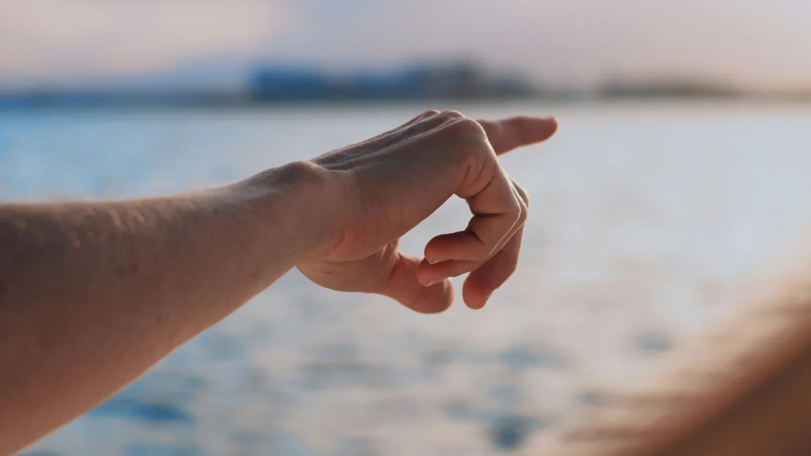 Foto zeigt ausgestreckten Arm und zeigendem Finger , im Hintergrund ein See